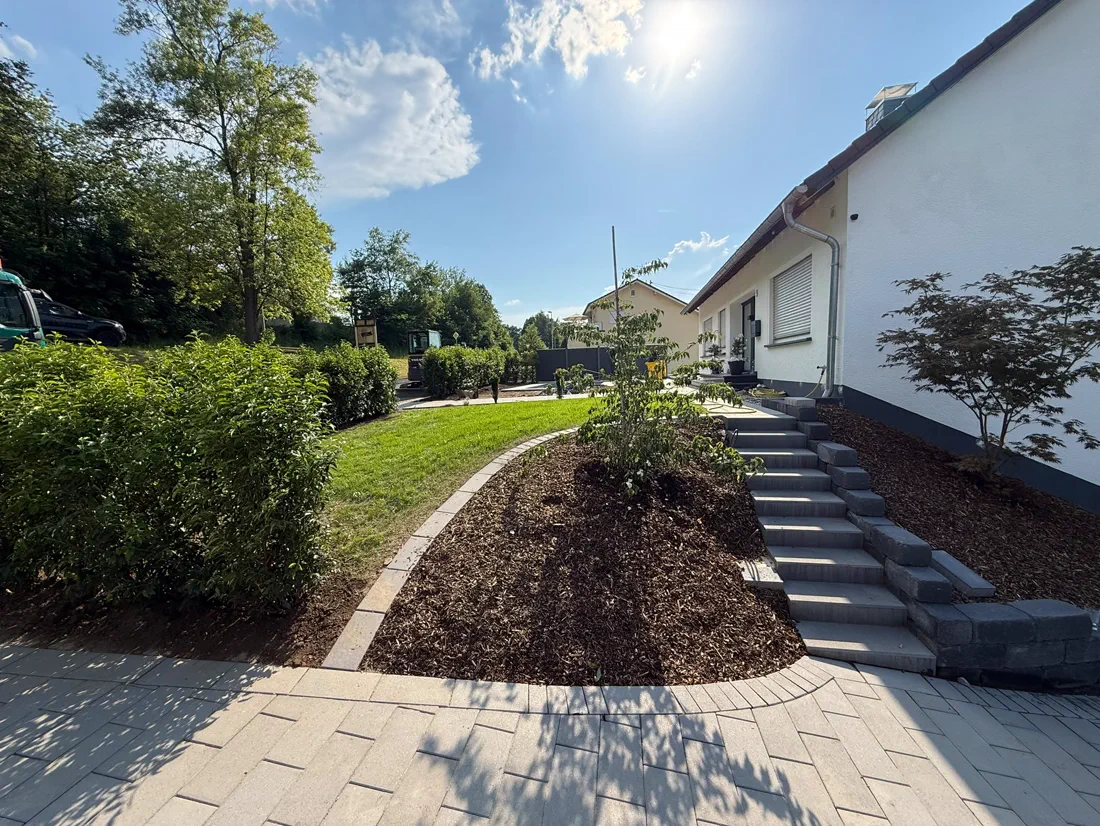 Fertige Außenanlage mit Mulchbeet, Treppenanlage und geschwungenem Plattenweg am Wohnhaus