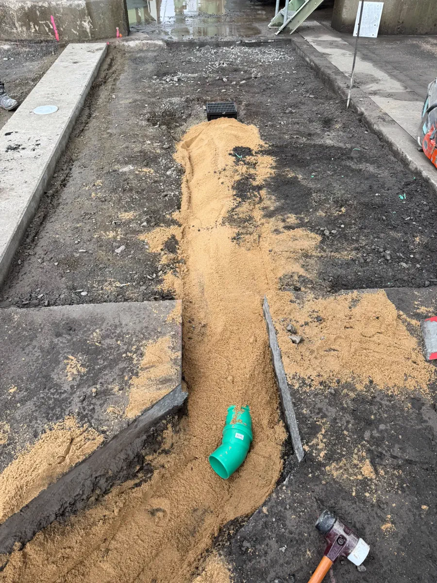 Schmaler Leitungsgraben im Sandbett zwischen Beton- und Pflasterfläche