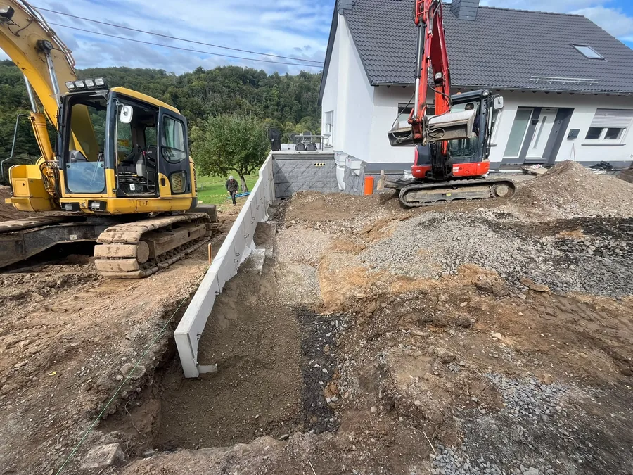 Gesetzte L-Steine als Stützmauer zwischen zwei Baggern auf einer Baustelle neben einem Wohnhaus