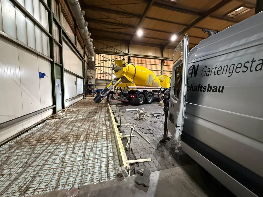 Fahrmischer betoniert die bewehrte Bodenplatte, rechts steht der Firmentransporter