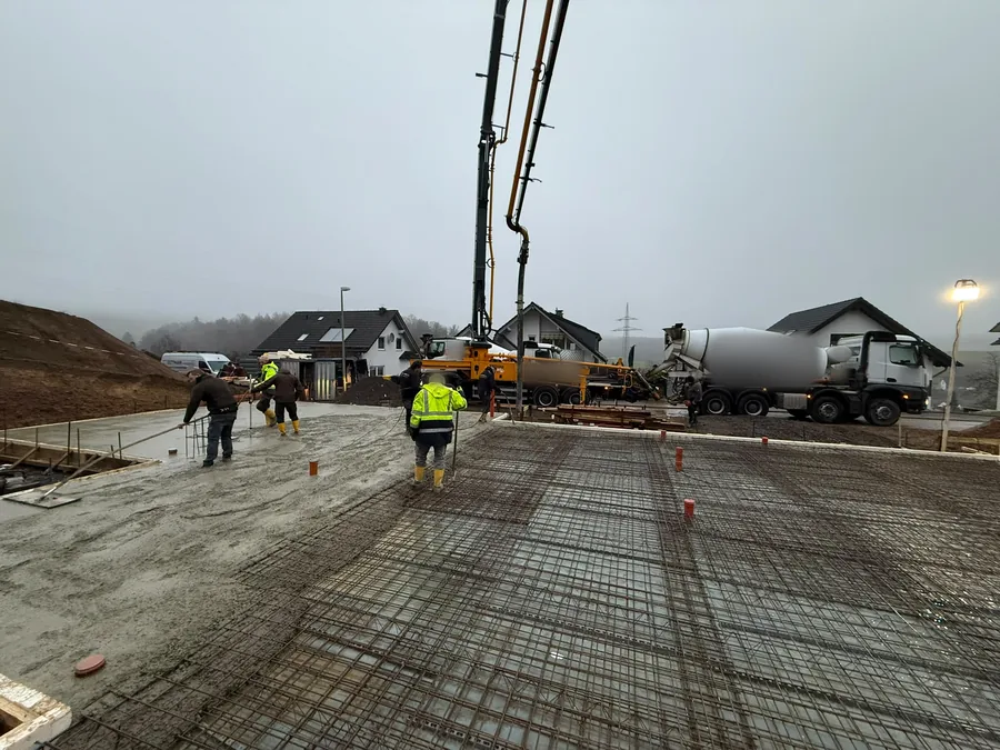 Frischer Beton wird auf einer bewehrten Bodenplatte verteilt, im Hintergrund Betonpumpe und Fahrmischer