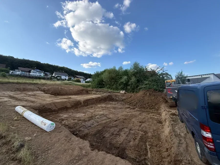 Ausgehobene Baugrube am Hang neben dem Haus, Vliesrolle im Vordergrund