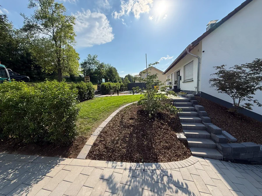 Dieselbe Außenanlage aus anderem Winkel: Mulchbeet, Treppe und geschwungener Plattenweg