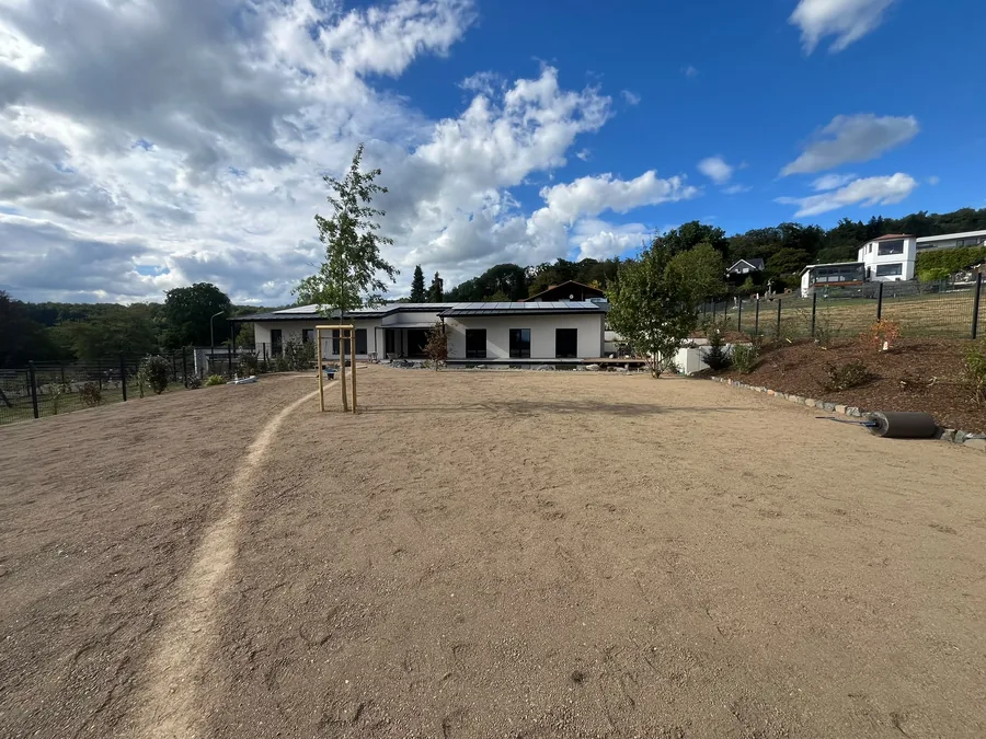 Fein planierte und für die Rasenansaat vorbereitete Gartenfläche vor einem Bungalow, rechts eine Rasenwalze