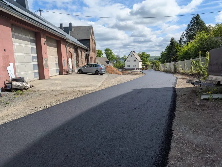 Frisch eingebaute Asphaltzufahrt führt an einem Backsteingebäude mit Rolltoren vorbei