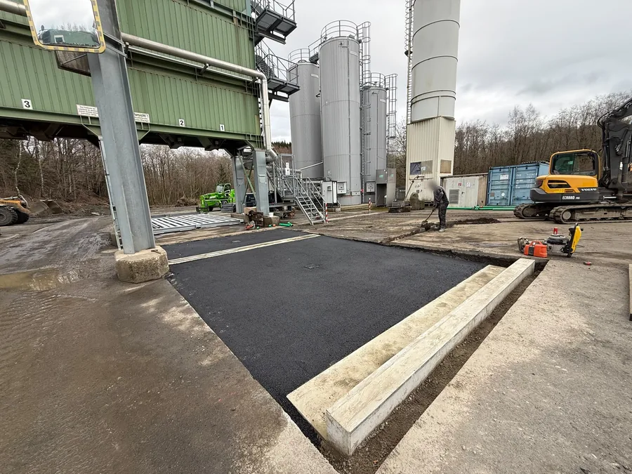 Frisch eingebaute Asphaltfläche mit Betonrinne, rechts ein Kettenbagger