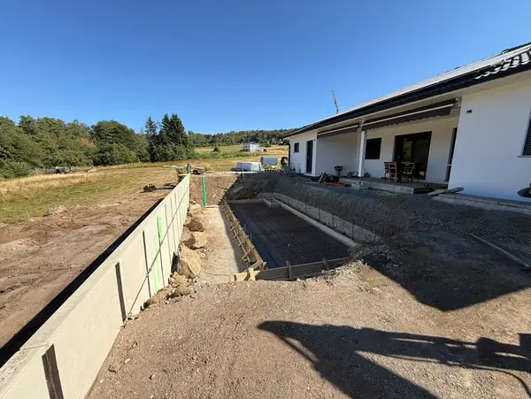 Ausgehobener Graben mit bereits gesetzten Beton-Winkelstützen vor einem Neubau-Bungalow
