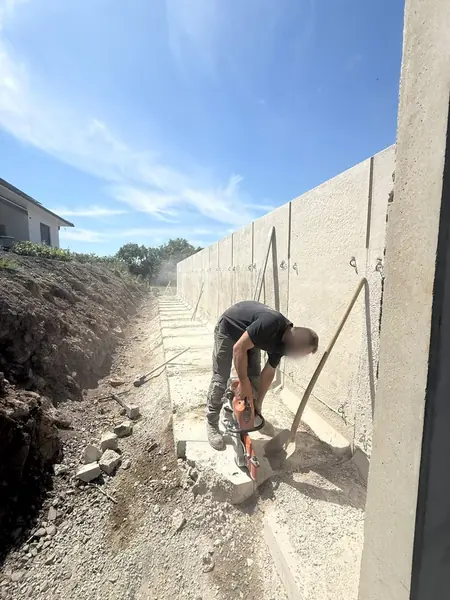 Randstein wird mit dem Trennschleifer am Fuß einer Winkelstützmauer aus Betonfertigteilen abgelängt