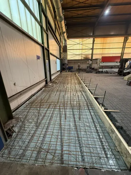 Bewehrungsmatten liegen auf Folie in der Schalung einer Bodenplatte entlang einer Gebäudewand