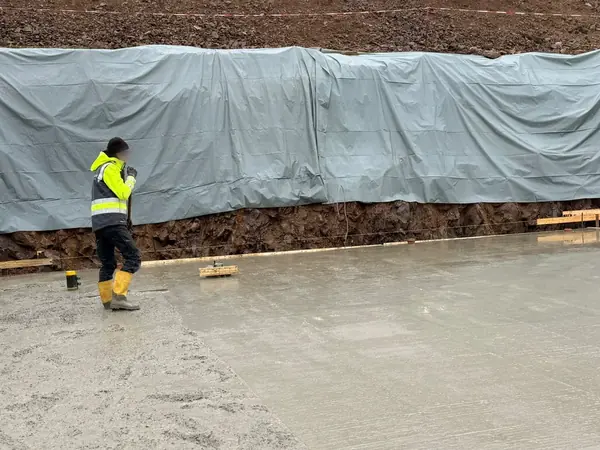 Frisch geglättete Betonbodenplatte, die Böschung dahinter ist mit Folie abgedeckt