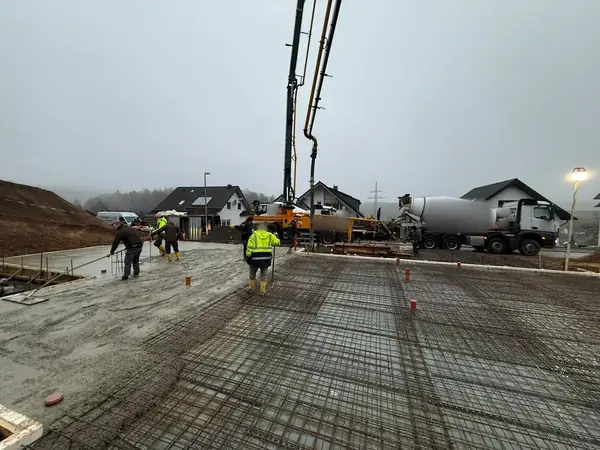 Frischer Beton wird auf einer bewehrten Bodenplatte verteilt, im Hintergrund Betonpumpe und Fahrmischer