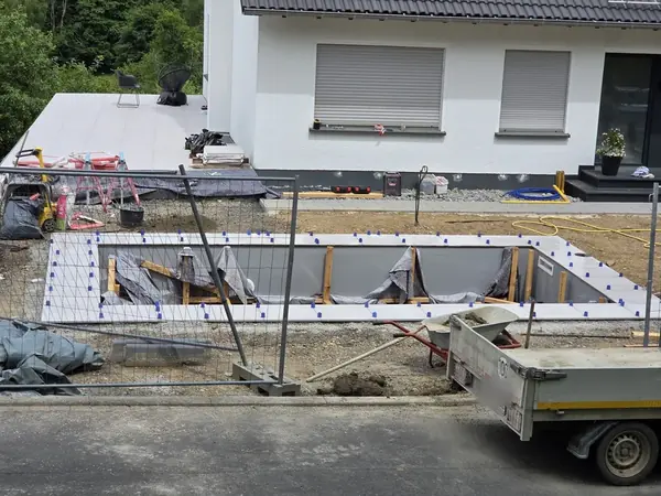 Poolbecken in Schalung mit Dämmelementen neben einer neu verlegten Terrasse an einem Wohnhaus