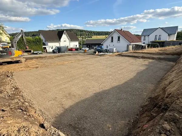 Verdichtetes Planum einer Baustelle im Wohngebiet, links steht ein Kettenbagger am Rand des Aushubs