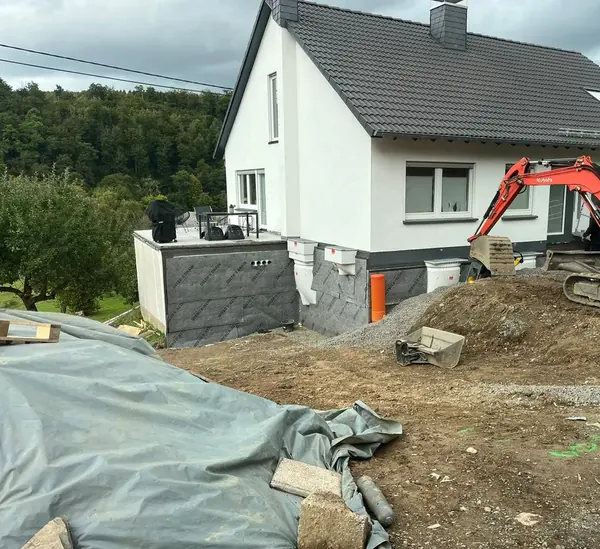 Minibagger profiliert das Gelände an einem Wohnhaus mit abgedichteter und gedämmter Kellerwand
