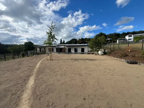 Fein planierte und für die Rasenansaat vorbereitete Gartenfläche vor einem Bungalow, rechts eine Rasenwalze
