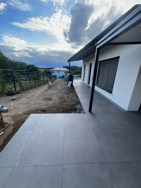 Neu verlegte großformatige Terrassenplatten entlang eines Hauses, daneben eine planierte Fläche für die Rasenansaat