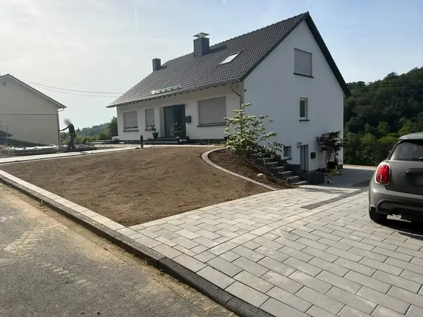Fertig gepflasterte Einfahrt mit Randeinfassung, frisch angesäter Vorgartenfläche und bepflanztem Beet