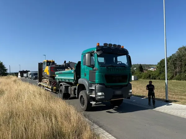 Kipper des Betriebs zieht einen Tieflader mit Kettenbagger über eine Ortsstraße