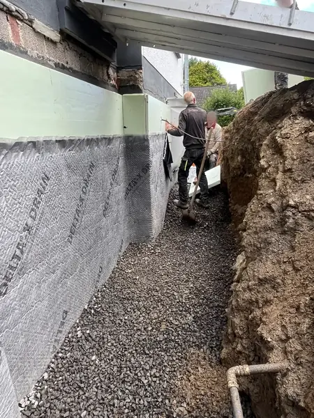 Arbeitsgraben an einer mit Noppenbahn abgedichteten Kellerwand, der Graben ist mit Drainagekies verfüllt